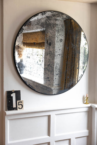 A large round antique-style mirror on a white wall, styled with some decorative numbers and a candlestick holder.