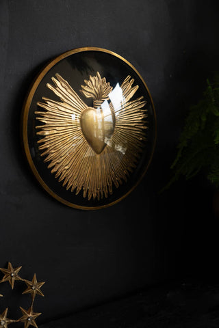 The Framed Golden Milagro Heart Decoration displayed on a dark wall, styled with a star ornament and some greenery.