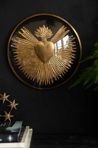 The Framed Golden Milagro Heart Decoration styled on a dark wall above a star ornament, books and a plant.