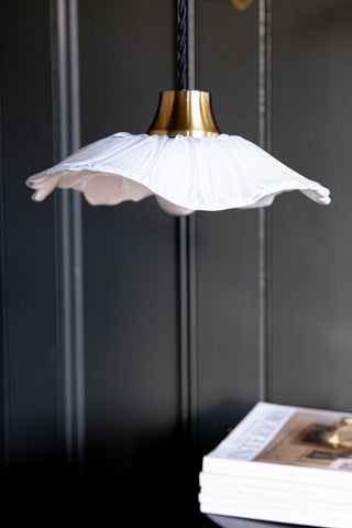 The Frosted Flower Daisy Glass Easyfit Ceiling Light Shade displayed hanging in front of a dark wall above some magazines.