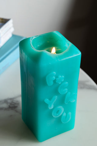 Close-up of the lit Fuck You Candle with wax that has dripped down the side, displayed on a white marble table.