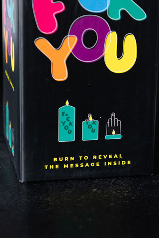 Close-up of the box of the Fuck You Candle on a dark surface.