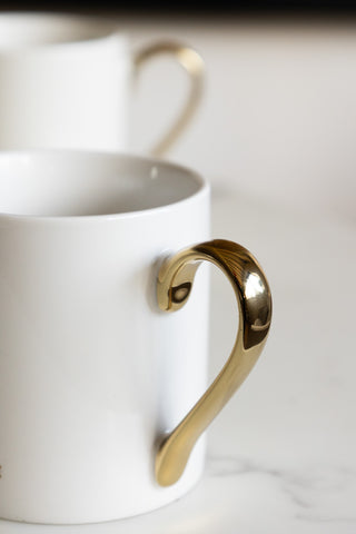 The gold handle of a white mug 