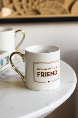 A white ceramic statement mug featuring a large gold handle 