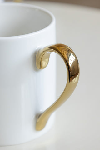 A close-up of a metallic gold handle on a white mug