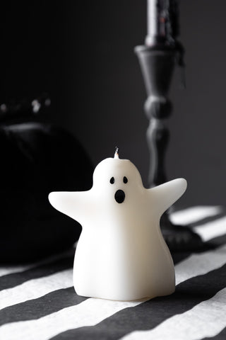 The Ghost Shaped Candle styled on  a stripe tablecloth in front of a pumpkin and candlestick holder.