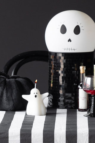 The Ghost Shaped Candle styled on a table with halloween decorations, a bottle and a glass.