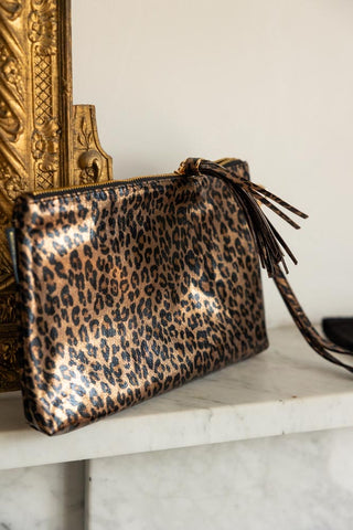 The Glam Leopard Print Clutch Bag displayed on a shelf next to an ornate gold frame.