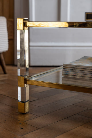 Close-up of the side of the Gold & Glass Coffee Table, styled with a stack of magazines on the lower shelf.