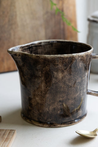 A side view of a glazed black and brown ceramic jug 