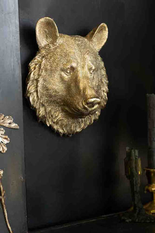 A wall ornament in the shape of a bear's head, displayed on a black wall, styled with some candles.