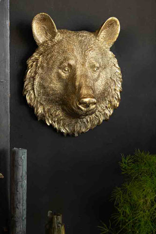 A bear head wall ornament on a black wall, above some candles and a plant.