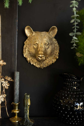 A bear head ornament styled on a black wall, surrounded by greenery, candles and a jug.