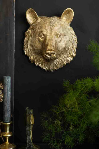 A gold bear ornament on a black wall above some candles and a plant.