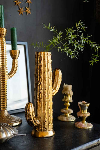 The Gold Cactus Stem Vase styled with greenery inside on a black sideboard, with candlestick holders and a framed print.