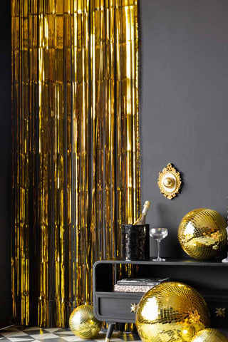 The Gold Curtain styled on a black wall, next to a black unit styled with disco balls and party accessories.