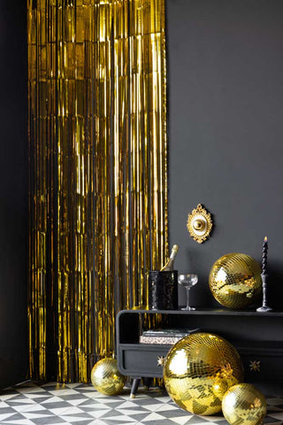 The Gold Curtain styled on a black wall next to various black and gold party decorations and home accessories.