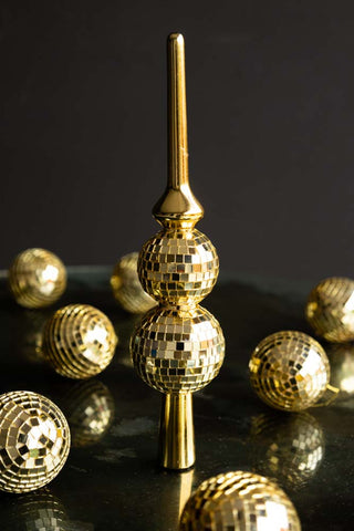 A Gold Disco Ball Tree Topper styled with lots of matching gold disco ball Christmas tree ornaments, on a dark surface.