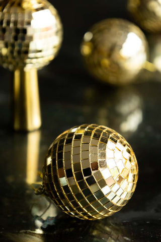 Close-up of a gold disco ball Christmas tree decoration on a dark surface, with multiple other decorations in the background of the shot.