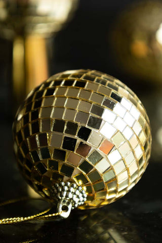 Close-up of a Gold Disco Ball Christmas Tree Decoration on a dark surface.