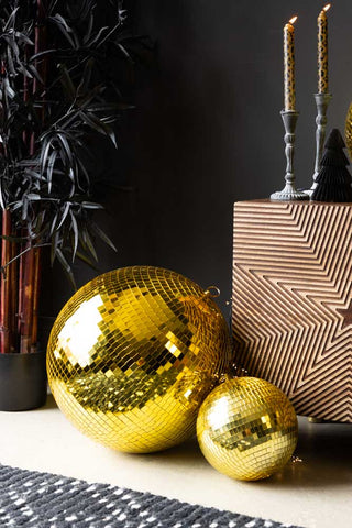 The Gold Disco Ball - 20cm styled on the floor together with a larger version, next to a rug, plant and wooden unit.