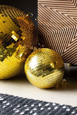 The Gold Disco Ball - 20cm styled with a larger version, on the floor next to a storage unit and rug.