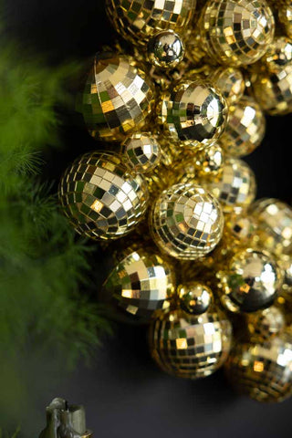 Close-up of the Gold Disco Ball Wreath hanging on a dark wall next to a plant and candlestick holder.