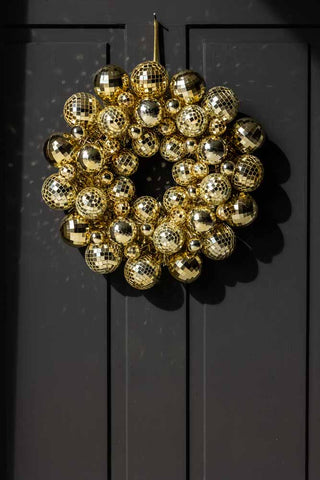 The Gold Disco Ball Wreath hanging on a black door, with the light casting reflections around it.