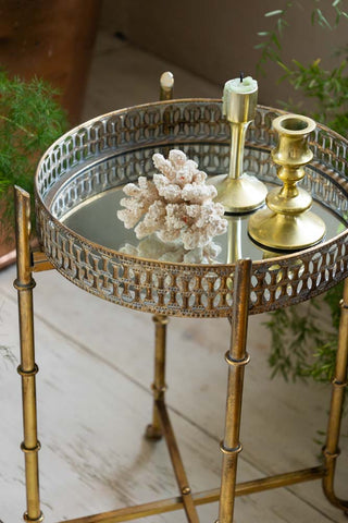 The Gold Distressed Mirrored Side Table with accessories on the top, styled with plants to the side.