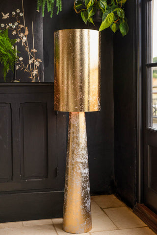 The Gold Leafed Effect Floor Lamp switched on and displayed in the corner of a black room.