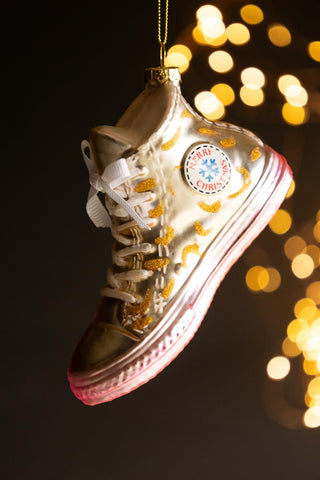 The Gold Glass Sneaker Christmas Tree Decoration hanging in front of a dark background with fairy lights.