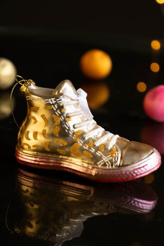 The Gold Glass Sneaker Christmas Tree Decoration displayed on a dark surface with Christmas decorations and fairy lights.