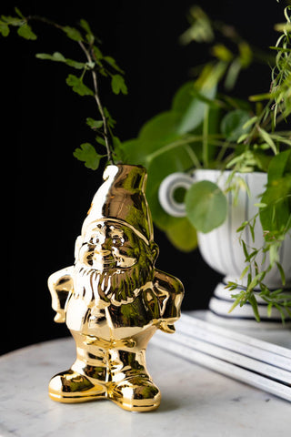 The Gold Gnome Single Stem Vase / Candlestick Holder styled with greenery inside, with magazines and a planter in the background.