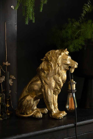 The Quirky Gold Lion Lamp switched off, styled on a black sideboard with greenery and candles.