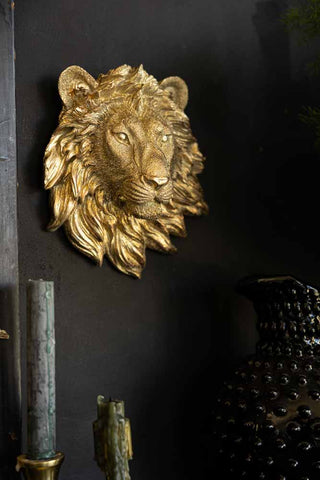 A gold lion head ornament on a black wall, above some candles and a jug.