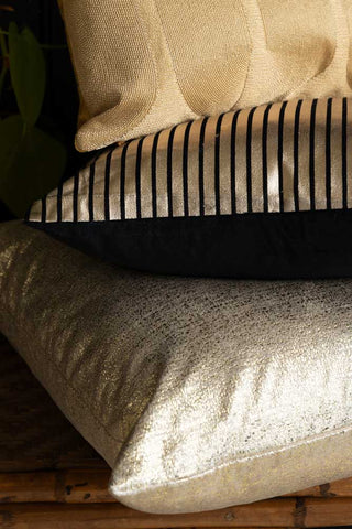 The Gold Metallic Velvet Cushion on a wicker bench, with other cushions arranged on top.