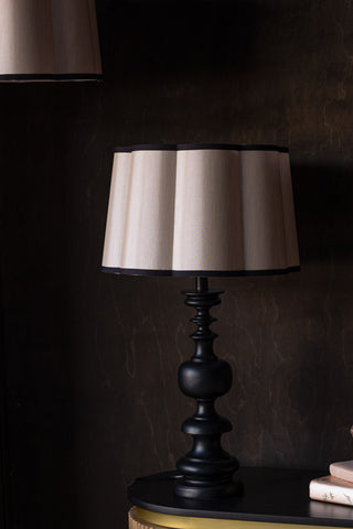 The Oyster Scalloped Easyfit Lampshade styled on a lamp base, on a wooden unit with some books, with another lampshade in the corner of the shot.