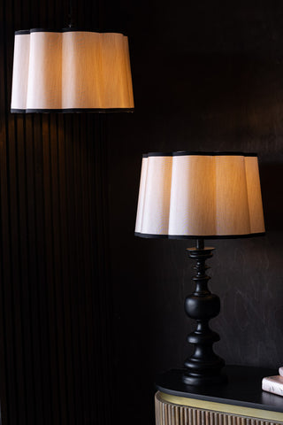 Two Oyster Scalloped Easyfit Lampshades, one on a lamp base styled on a wooden unit with some books and the other hanging as a pendant, both with bulbs illuminated inside.