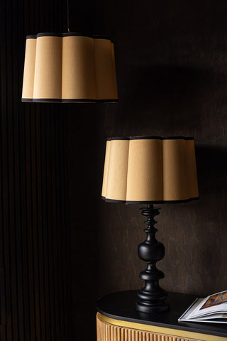 Two Gold Scalloped Easyfit Lampshades, one styled on a lamp base on a wooden unit with an open book, and the other suspended as a pendant light inb front of a dark wall.