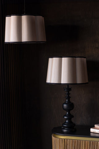 Two Oyster Scalloped Easyfit Lampshades, one styled as a pendant light in front of a dark wall and the other on a lamp base on a wooden unit, styled with some books.