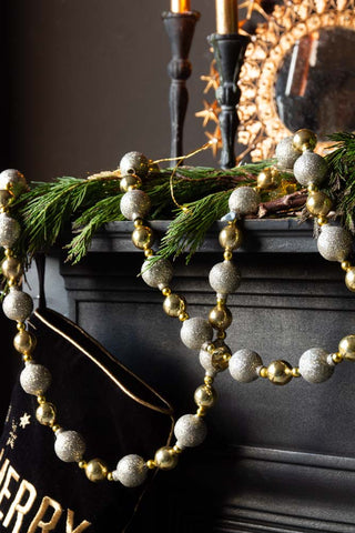 The Gold Sparkle Bauble Garland hung over a black mantlepiece above a black and gold stocking.