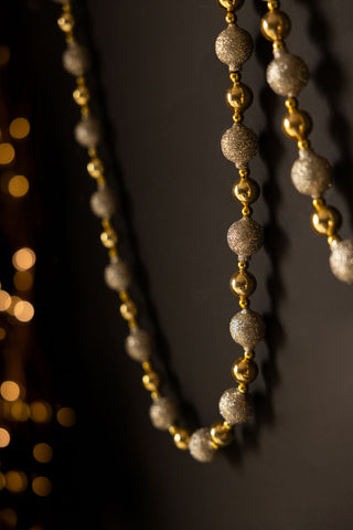 Detail shot of the Gold Sparkle Garland hanging in front of a black wall, with fairy lights in the background.