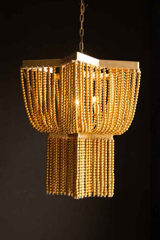 The Gold Star Shaped Beaded Statement Chandelier Light illuminated and hanging in front of a dark background.