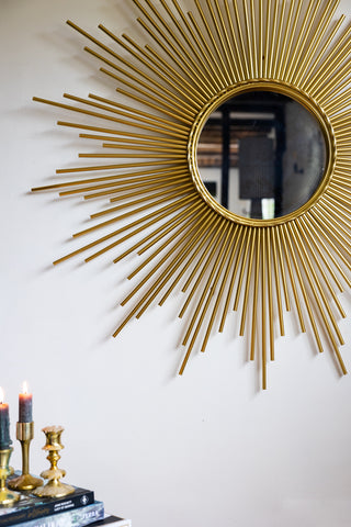 Close-up of a round mirror with a starburst design, displayed on a white wall above a table styled with candles and books.