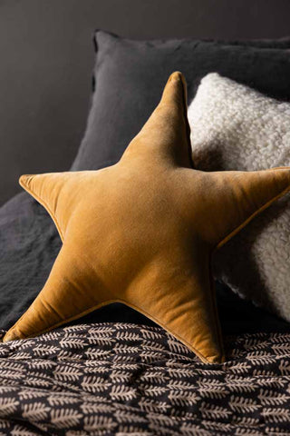 The Velvet Star Cushion In Gold styled on a bed with a quilt and a cushion.