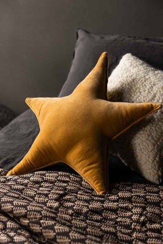 The Velvet Star Cushion In Gold displayed on a bed.