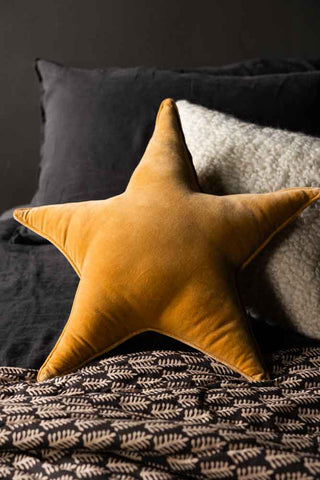 The Velvet Star Cushion In Gold styled on a bed with other soft furnishings.