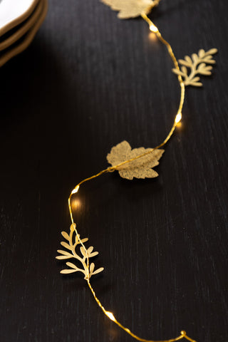 Golden leaf fairy lights turned on displayed on a Christmas table centrepiece.