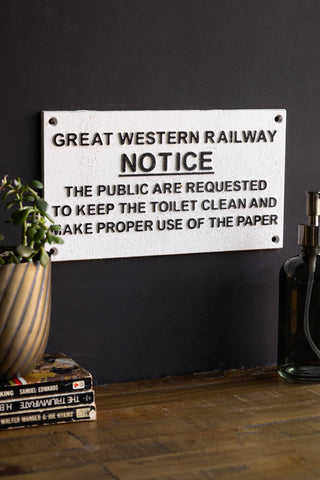 The Great Western Railway Notice Door Hanging Sign styled on a black wall above a wooden surface, with a potted plant on a stack of books and a soap dispenser.