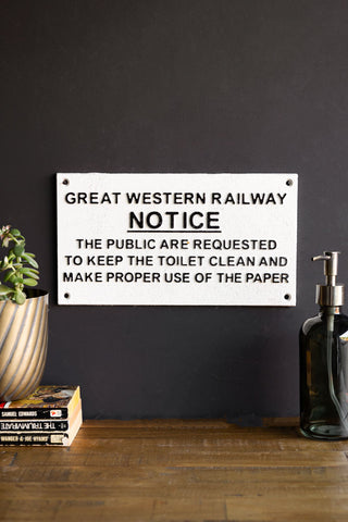 The Great Western Railway Notice Door Hanging Sign displayed on a black wall above a wooden surface, styled with a soap dispenser, stack of books and a potted plant.